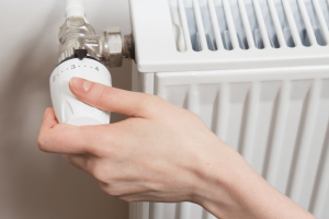 Mano che regola la valvola termostatica di un termosifone per controllare la temperatura del riscaldamento domestico