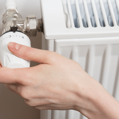 Mano che regola la valvola termostatica di un termosifone per controllare la temperatura del riscaldamento domestico