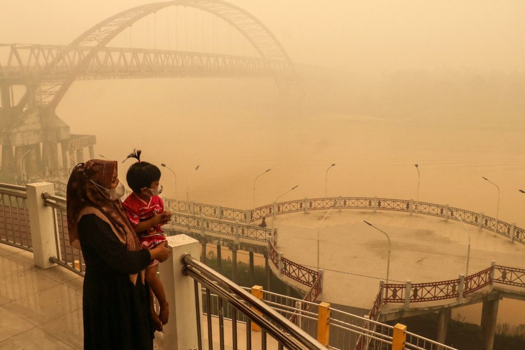 Una madre e un bambino con indosso mascherine osservano il panorama, immersi nella foschia causata dagli incendi boschivi in Indonesia